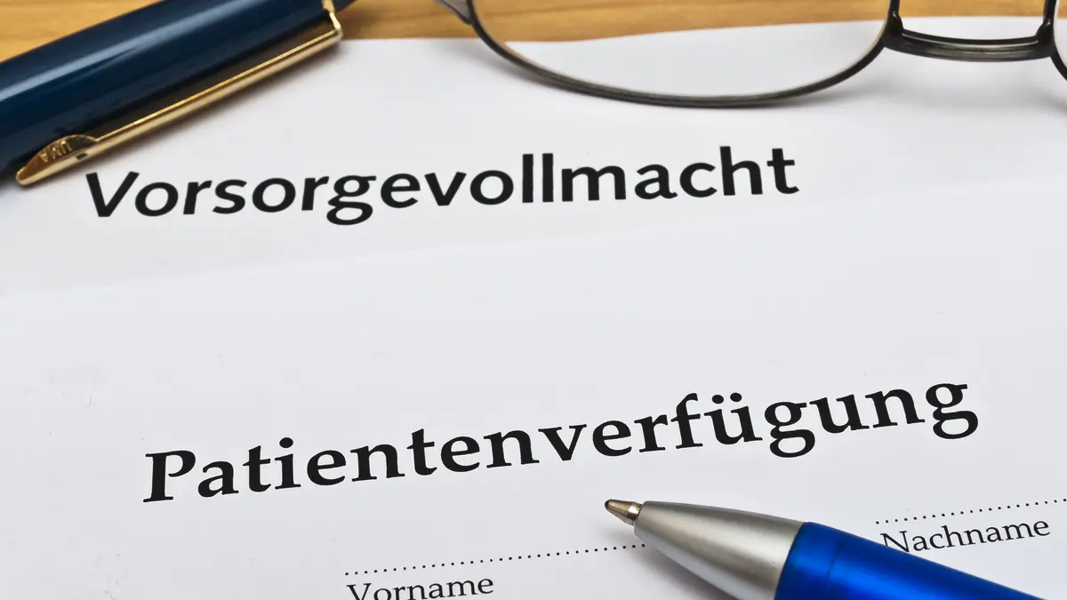 Ausdruck einer Patientenverfügung und eines Vorsorgevollmacht neben zwei Stiften und einer Brille auf einem Tisch