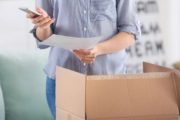 Frau hält Smartphone und öffnet ein Paket
