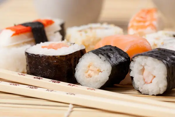 Sushirollen mit Lachs gefüllt liegen auf einer Sushimatte. Davor liegen zwei Essstäbchen.