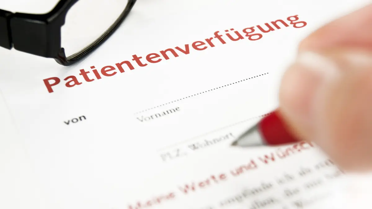 Eine Hand mit Stift zeigt auf ein Dokument, auf dem Patientenverfügung steht.