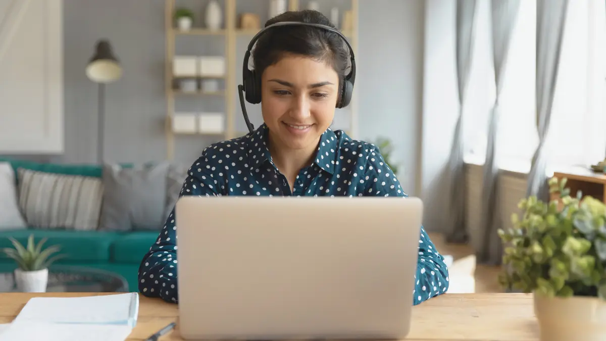 Eine Frau mit Headset sitzt in einem großen Zimmer am Laptop.