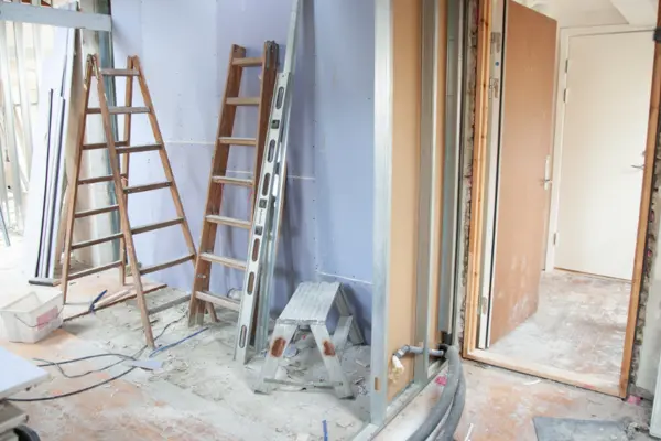 Leitern und Werkzeuge lehnen an einer Wand in einem Zimmer, das im Rohbau ist