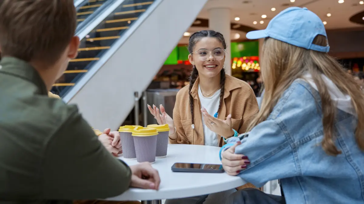 Jugendliche sitzen in Einkaufszentrum mit Kaffeebechern