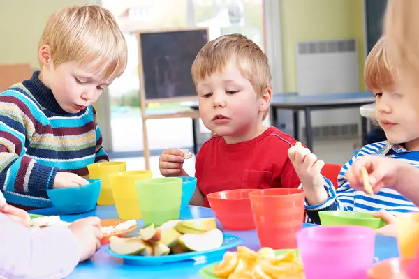 Mehrere Kinder sitzen am Tisch in der Kita und essen Obstschnitze 