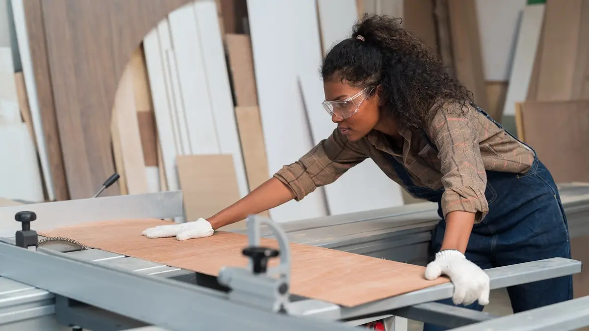 Eine Frau schneidet an einer Werkbank ein Stück Holz