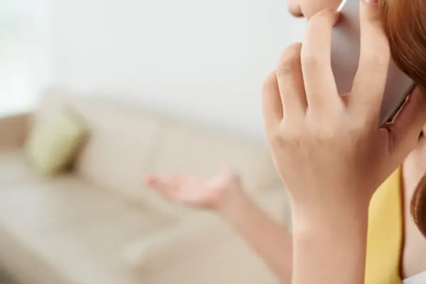 Eine junge Frau telefoniert und hebt eine Hand als Geste der Ratlosigkeit
