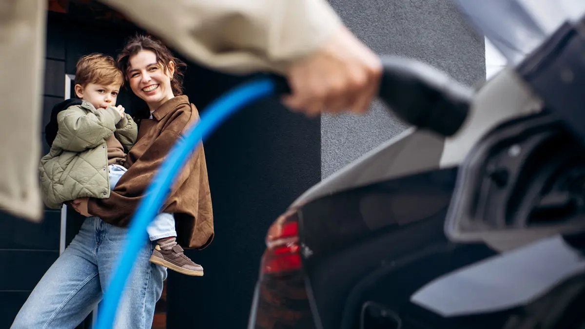 Familie stehen neben einem schwarzen Elektro-Auto, das an einer Ladestation geladen wird.