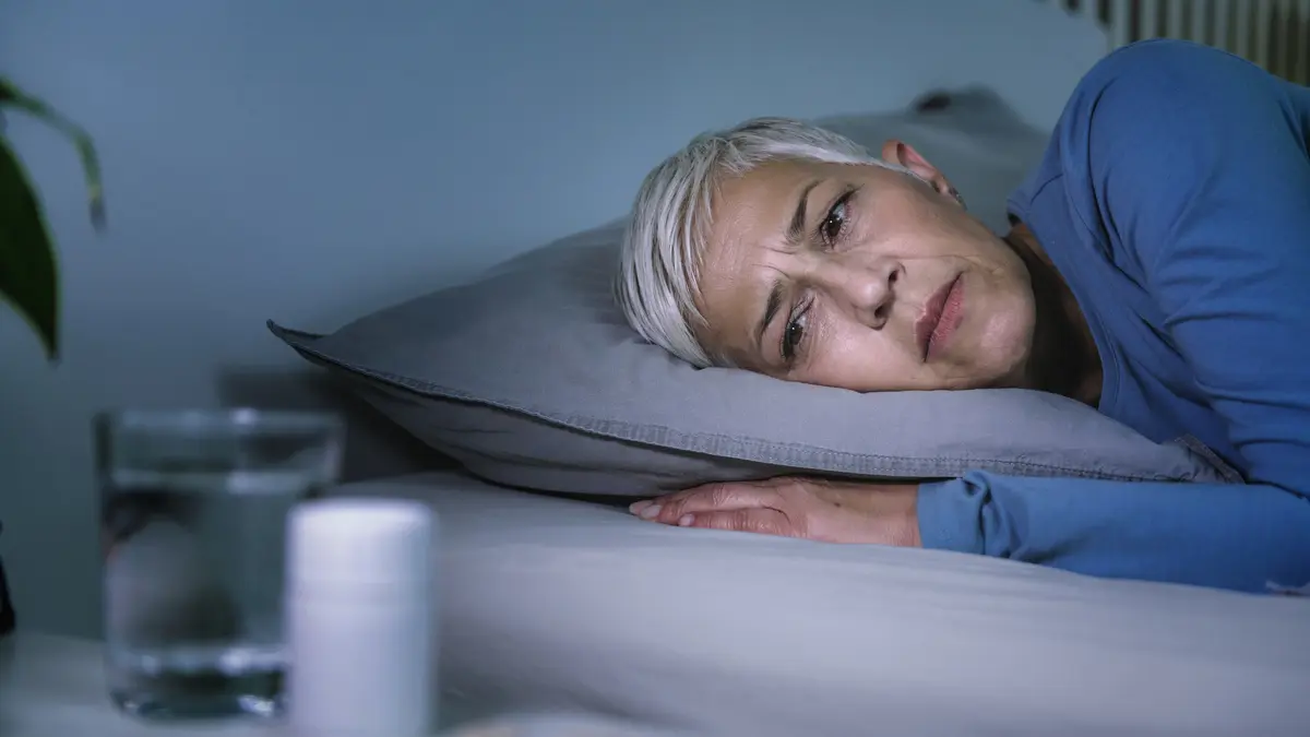 Eine schlaflose Frau liegt wach im Bett und schaut auf eine Dose mit Schlaftabletten