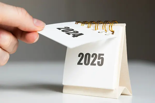 Hand reißt Kalenderblatt ab, sodass Jahreszahl 2025 zum Vorschein kommt