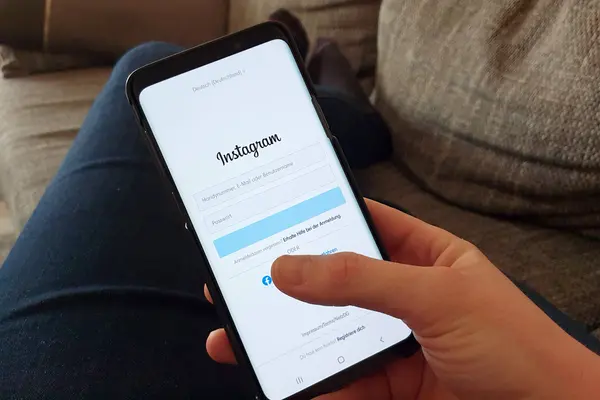 Foto aus der Perspektive einer Person, die auf einer Couch liegt und ein Smartphone in der Hand hält, das die Login-Seite von Instagram zeigt