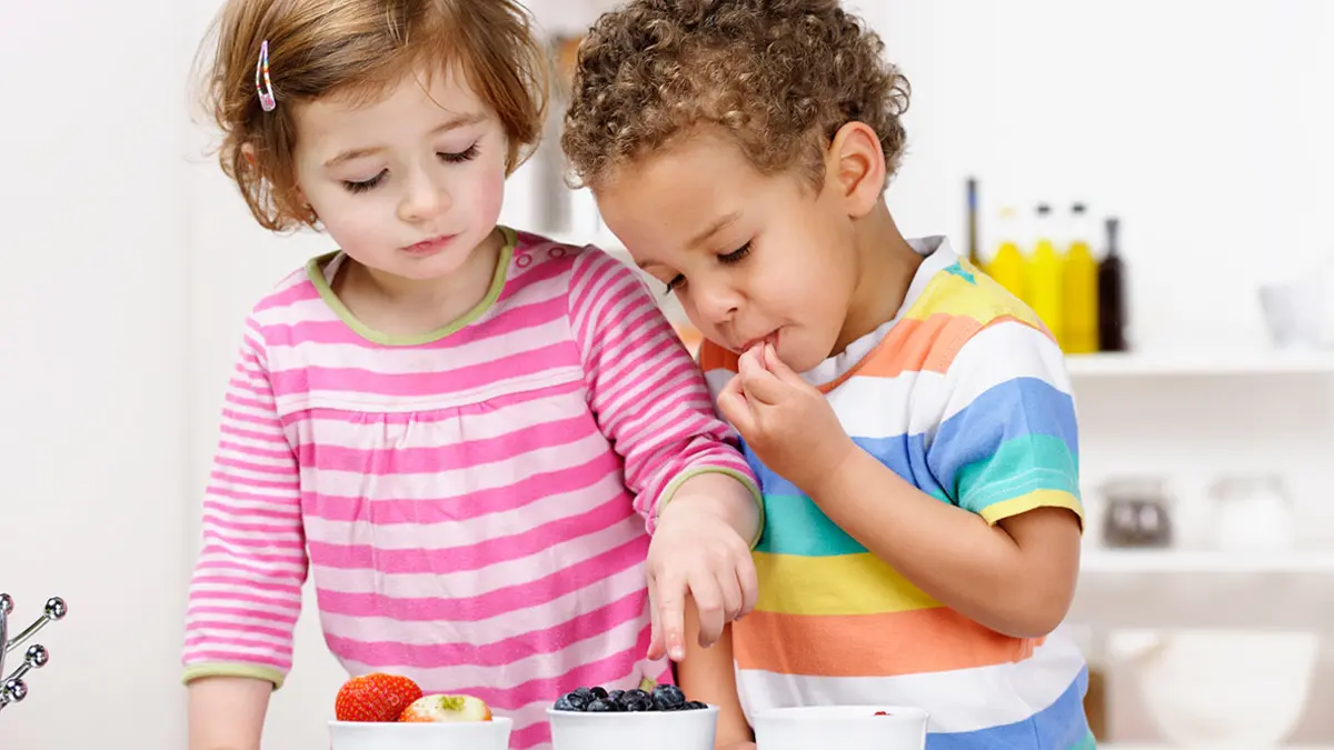 Kleines Mädchen und kleiner Junge essen verschiedene Obstsorten aus Schälchen