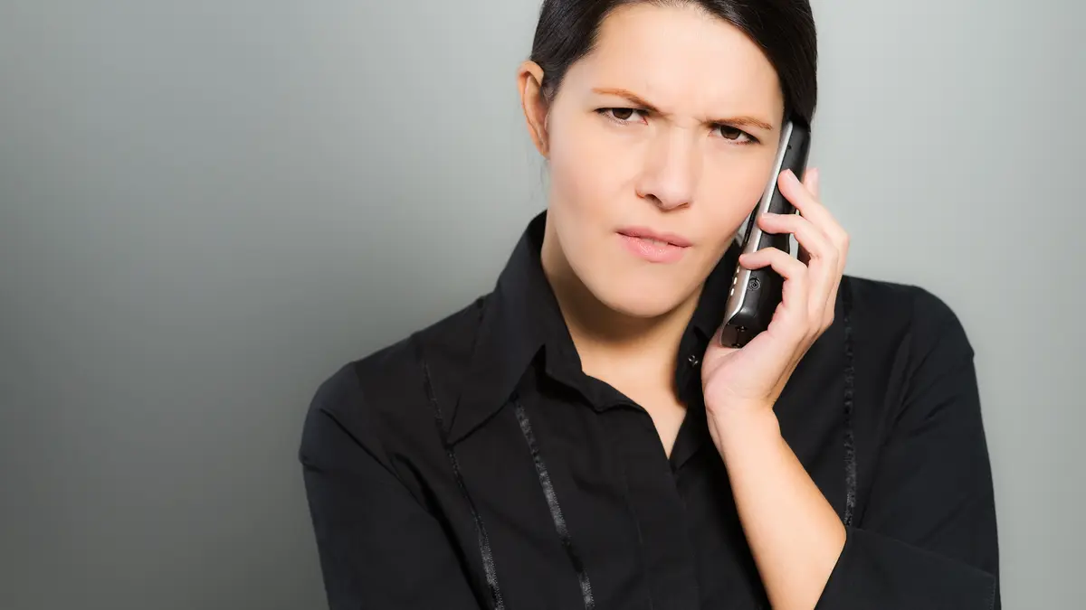 Eine Frau telefoniert und schaut dabei ernst.