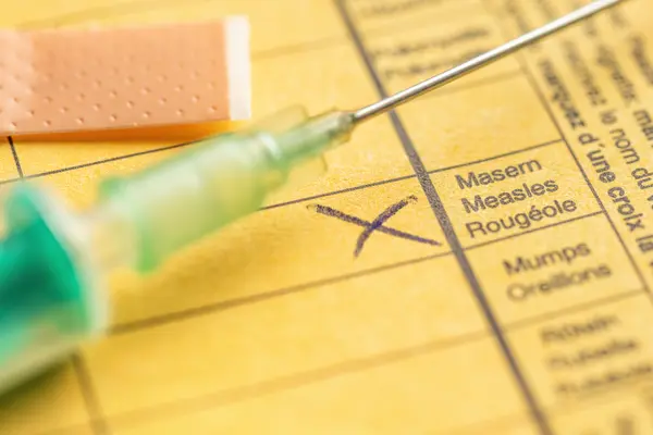 Eine Spritze mit Impfstoff gegen Masern liegt auf einem offenen Impfpass