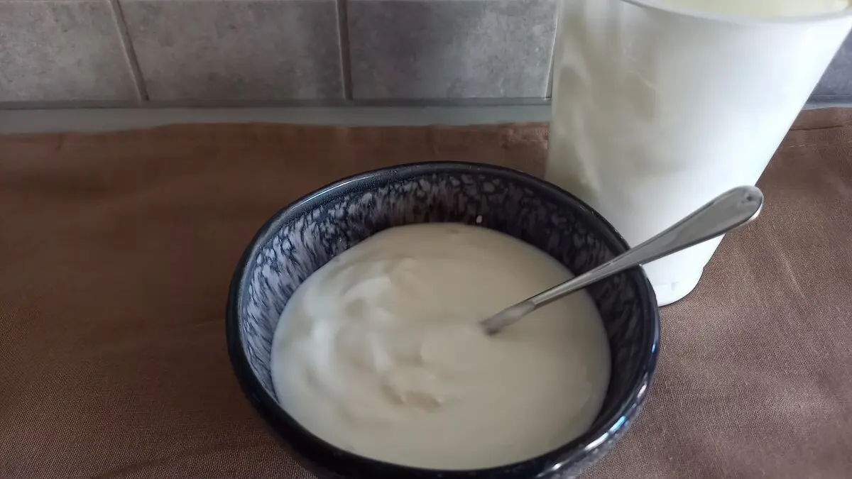 Eine schwarze Müslischüssel mit Naturjoghurt und einem Löffel darin steht auf einer Küchenarbeitsplatte
