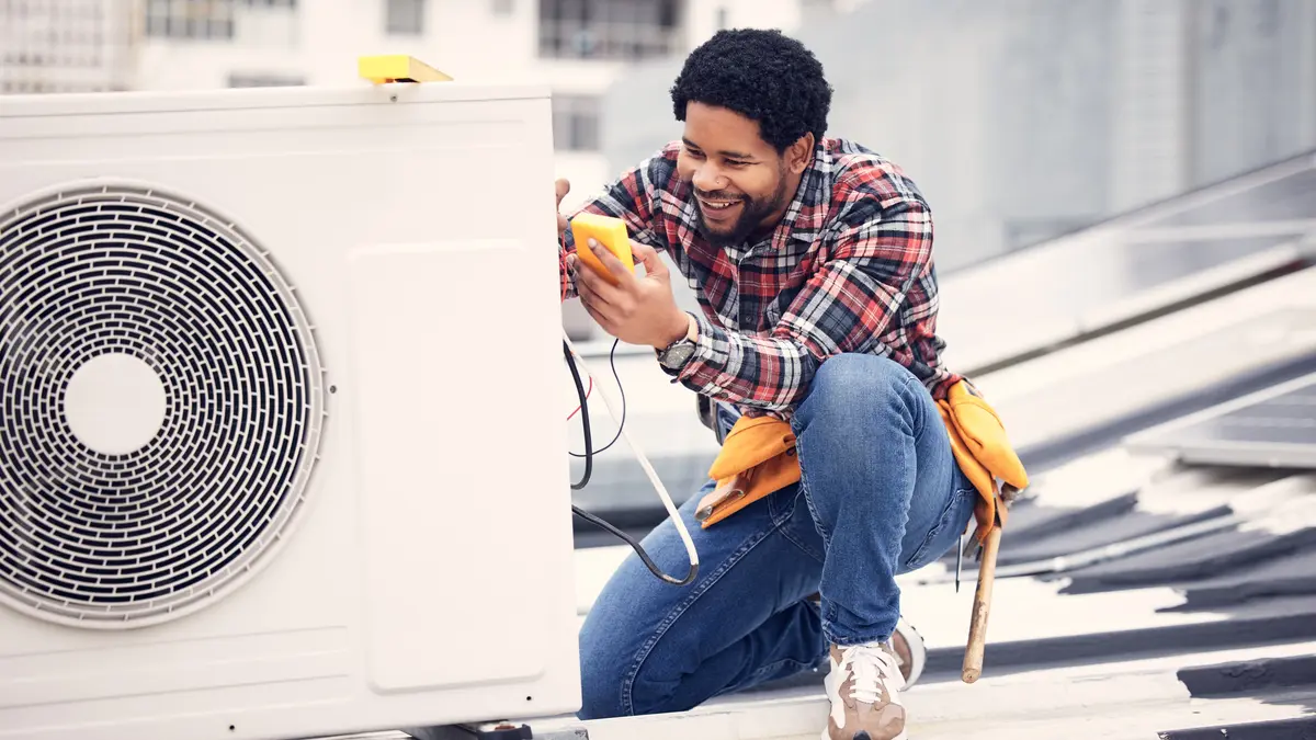 Ein freundlicher Techniker sitzt mit einem Testgerät neben einer elektrischen Wärmepumpe.