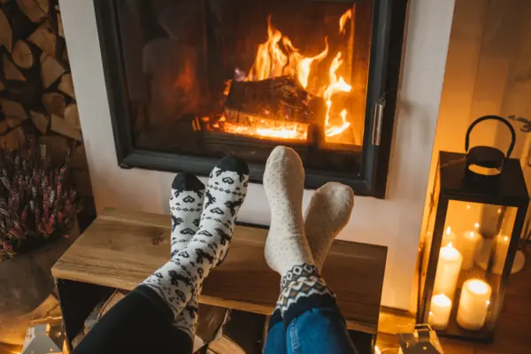 Füße vor einem Kamin, in dem ein Feuer brennt, gemütliche Atmosphäre