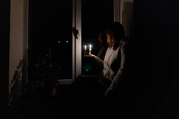Frau steht mit Kerze am Fenster