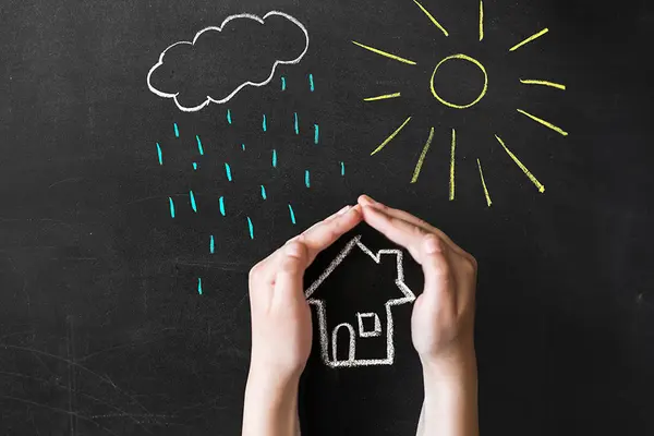 Hand schützt gezeichnetes Haus vor gezeichneten Regen- und Sonnenstrahlen