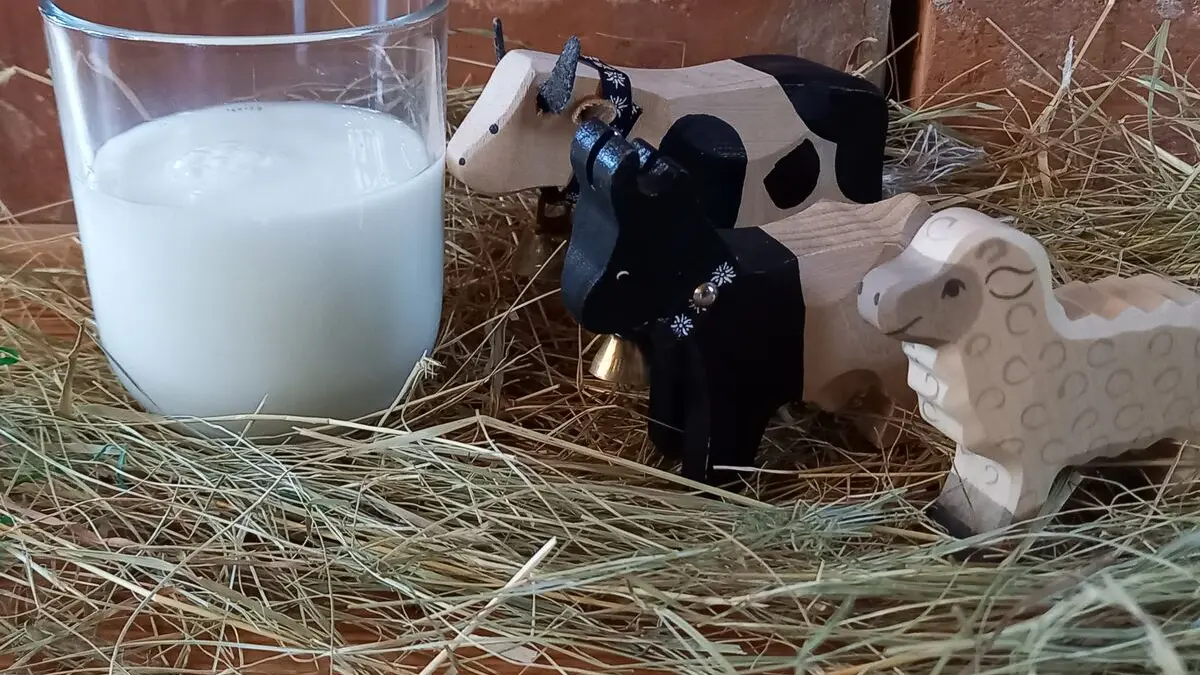 Kuh, Schaf und Ziege als Holzfiguren stehen neben einem Glas Milch.