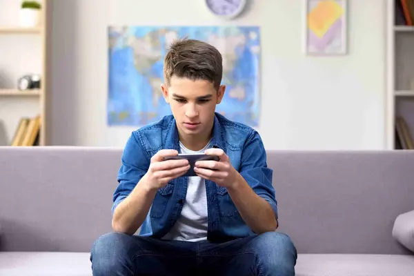 Junge sitzt auf Couch mit Handy in der Hand