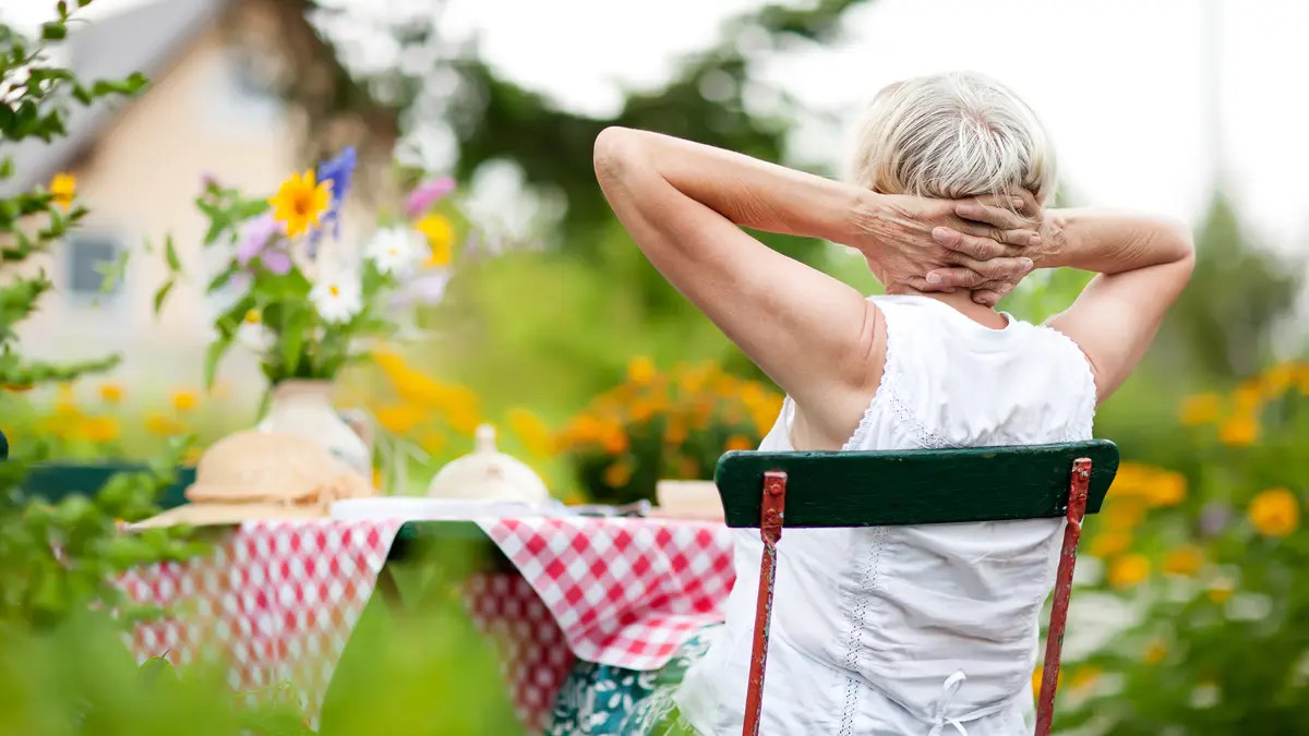 Seniorin sitzt im Garten und schaut Haus an