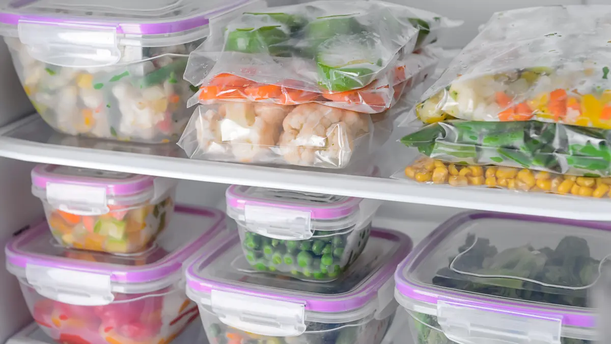 Behälter und Plastikbeutel mit gefrorenem Gemüse im Kühlschrank