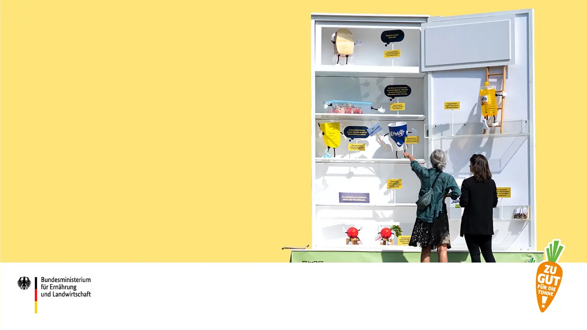 Zwei Frauen stehen vor einem überdimensionalen Kühlschrank.