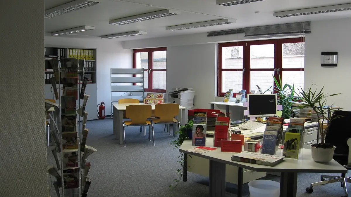 Ein menschenleerer Büroraum mit Schreibtischen und Prospektständern.