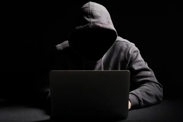 vermummte Person sitzt vor einem Laptop