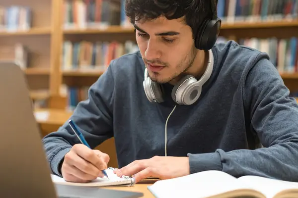 Ein Schüler sitzt in einer Bibliothek vor einem Laptop und lernt