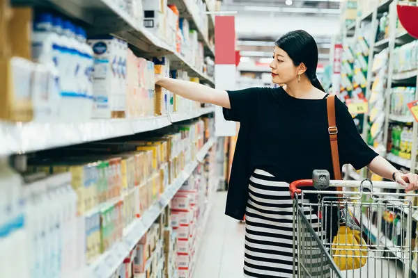 Schwangere Frau steht mit Einkaufswagen vor Supermarktregal