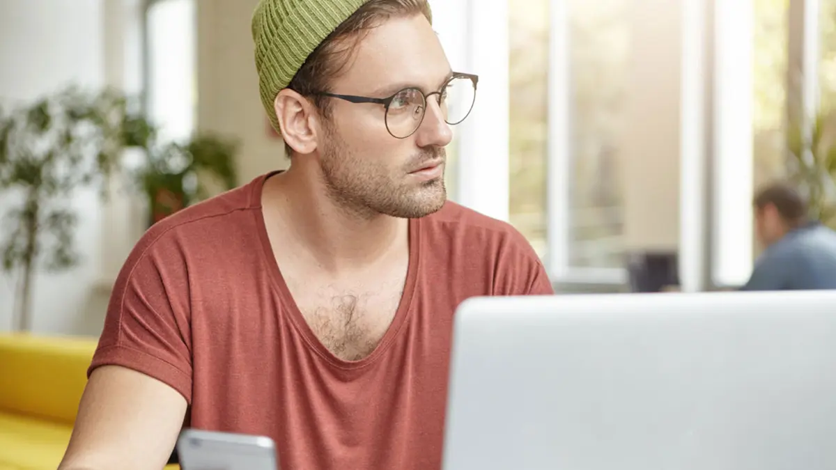 Ein Mann sitzt genervt vor seinem Laptop und schaut zur Seite