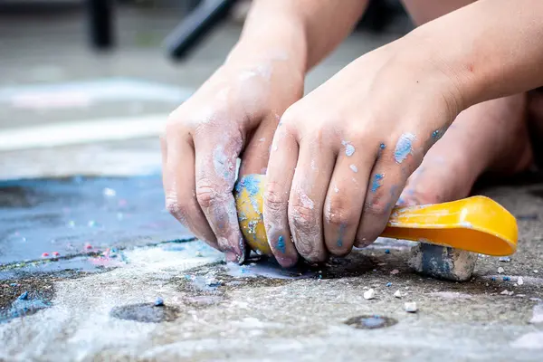Kinderhände spielen mit Schaufel und Straßenmalkreide