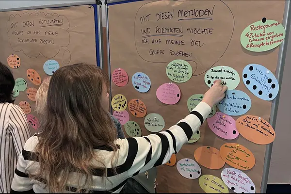 Eine Person pinnt bei einem Workshop ein Postit an eine Posterwand