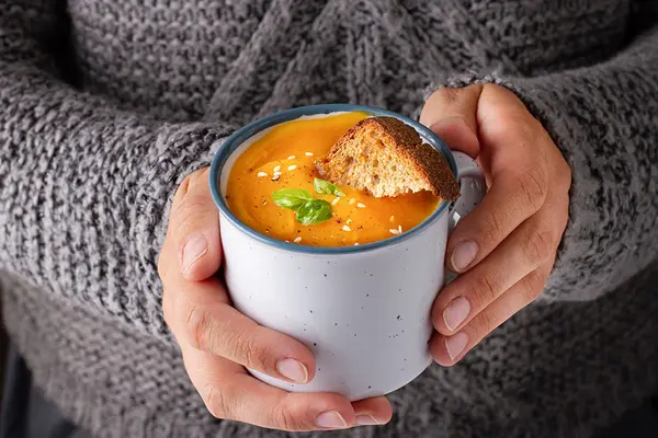 Jemand hält eine Tasse mit Suppe in den Händen