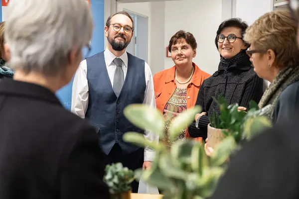 Drei Personen stehen im Raum und lächeln in die Kamera.