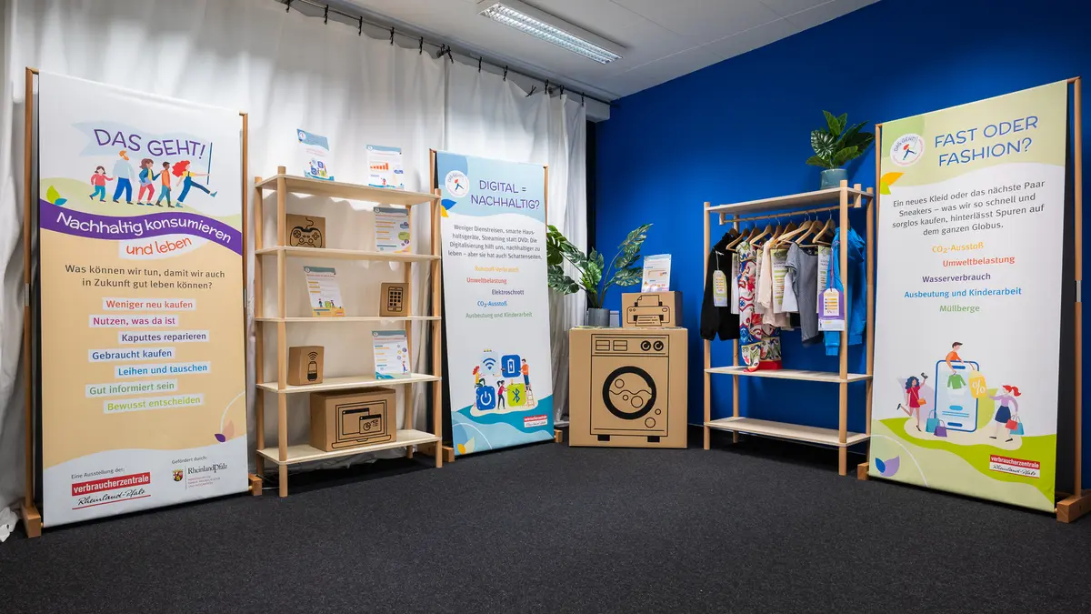 Die Wanderausstellung "Das geht! Nachhaltig konsumieren und leben" mit den drei Bannern, einem Regal und einem Kleiderständer