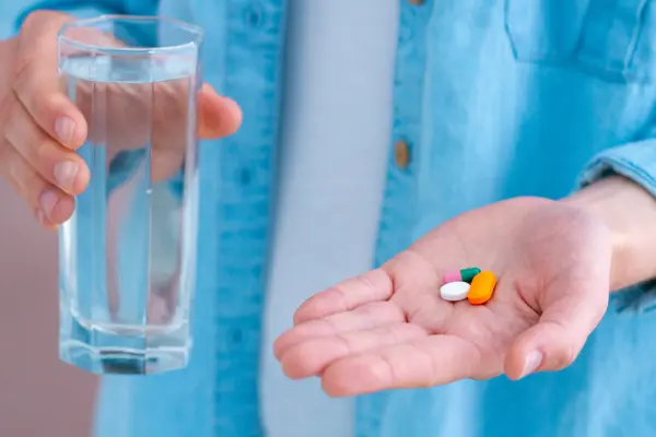 Jemand hält Tabletten in einer Hand und in der anderen ein Glas Wasser.