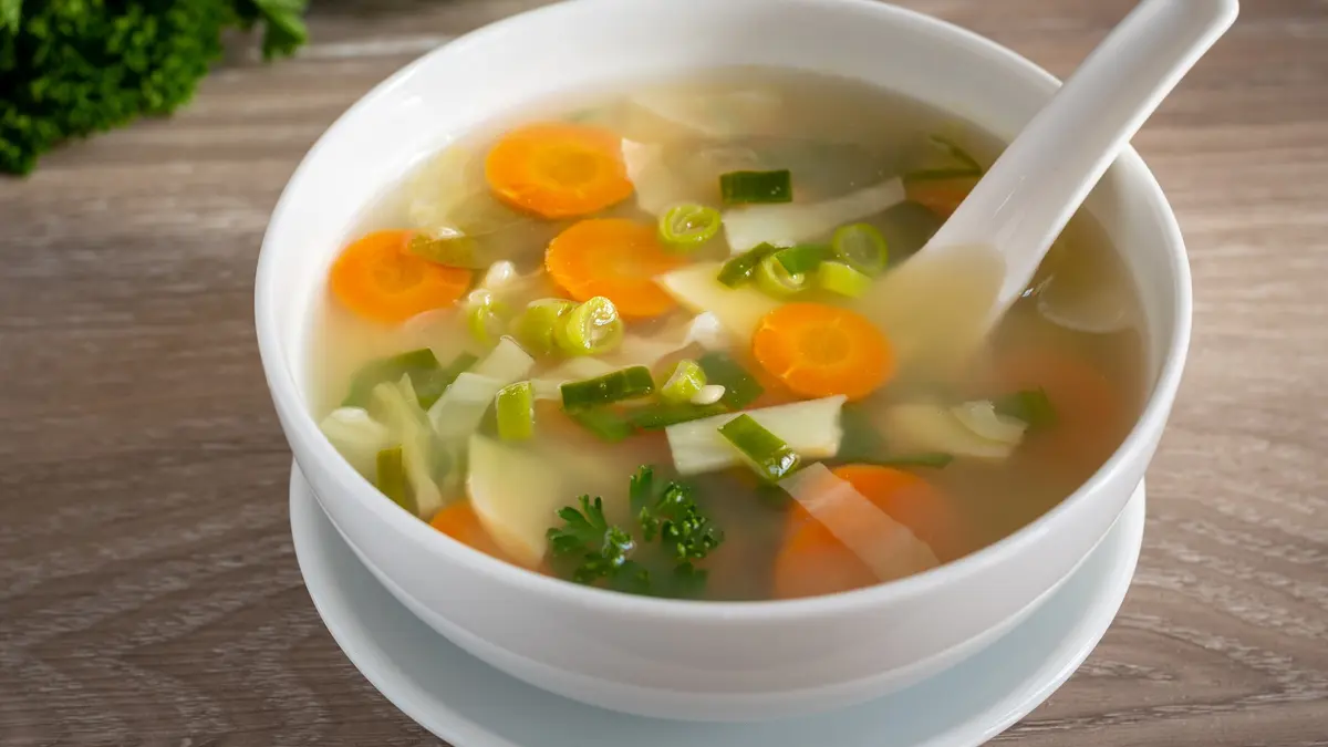 Ein Suppenteller mit einer Gemüsesuppe. Ein Löffel liegt bereits im Suppenteller.