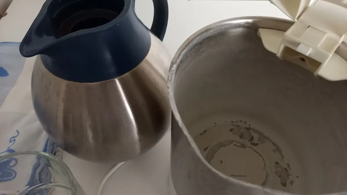 Neben einer Teekanne steht ein geöffneter Wasserkocher. In ihm sieht man deutliche Kalkspuren.