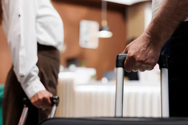 Zwei Gäste mit Rollkoffern gehen auf eine Hotelrezeption zu 