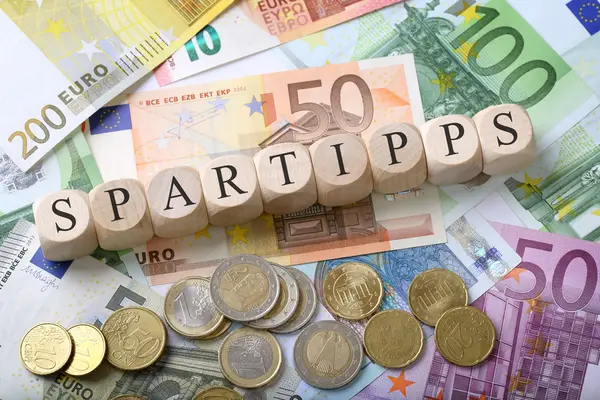 Würfel bilden das Wort Spartipps auf einem Haufen Geldscheinen und Münzen