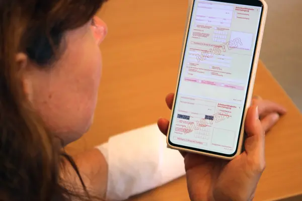 Frau hält Smartphone mit Arbeitsunfähigkeitsschein in der Hand