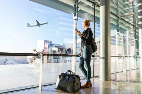 Frau schaut am Flughafen auf startendes Flugzeug