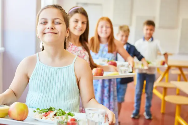 Lächelnde Studenten stehen in der Schlange und halten Tabletts mit Essen