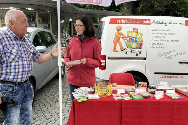 zwei unterhaltende Menschen vor dem Verbraucherzentralen Auto