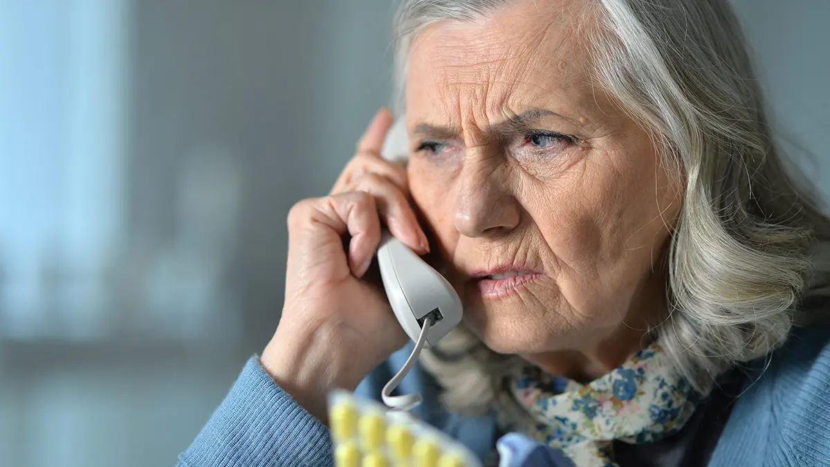 Ätere Dame hört am Telefonhörer kritisch zu