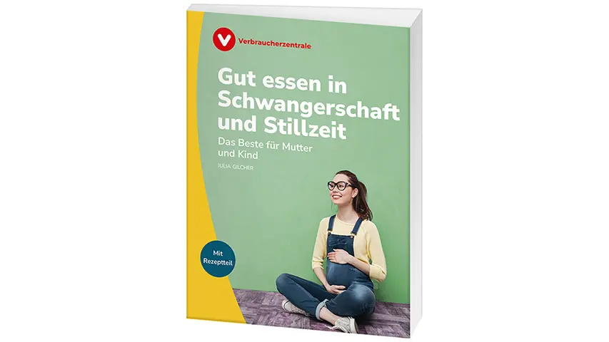 Schwangere Frau mit Brille sitzt im Schneidersitz auf dem Boden und hält sich mit einer Hand lächelnd den Bauch
