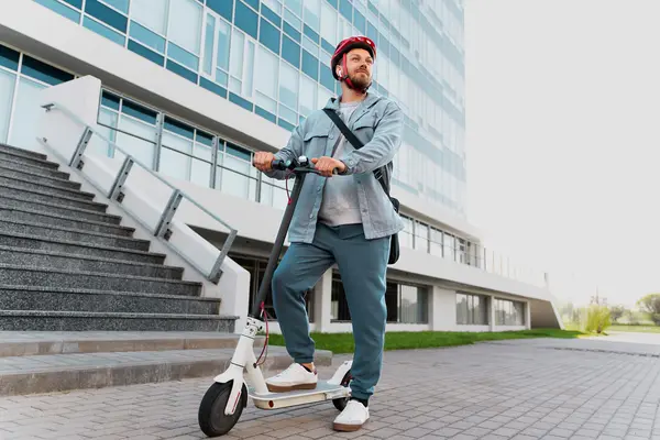 Ein Mann steht mit einem E-Scooter vor einem Bürogebäude