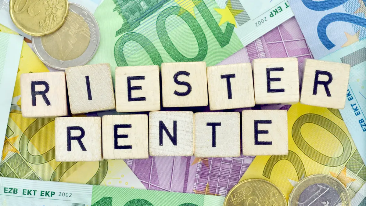Scrabble-Steine, die das Wort Riester-Rente bilden, liegen auf Geldscheinen und Münzgeld